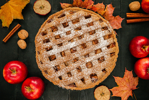 Delicious homemade apple pie, with apples, cinnamon sticks, decorative stars and fall leaves. Autumn Thanksgiving dinner flat lay composition on a wooden table.