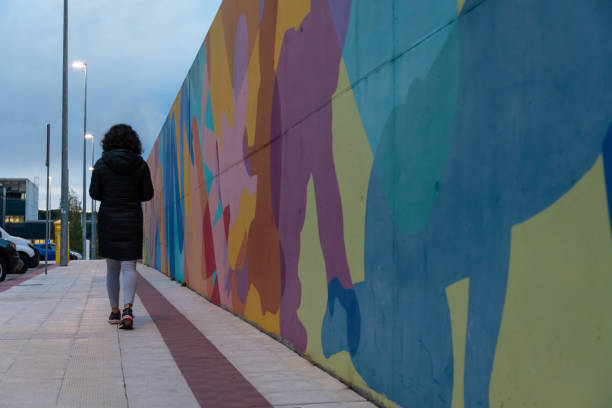 donna che cammina attraverso il quartiere al tramonto accanto al muro colorato - art coat full length foto e immagini stock