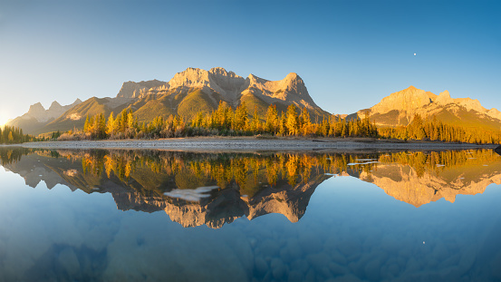Mountain landscape at dawn. Sunbeams in a valley. Rivers and forest in a mountain valley at dawn. Natural panoramic landscape with bright sunshine. Reflections on the surface of the lake. Banff National Park, Alberta, Canada.