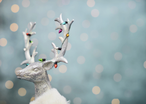 Modern Christmas background with silver deer wearing Christmas lights around antlers. Space for text