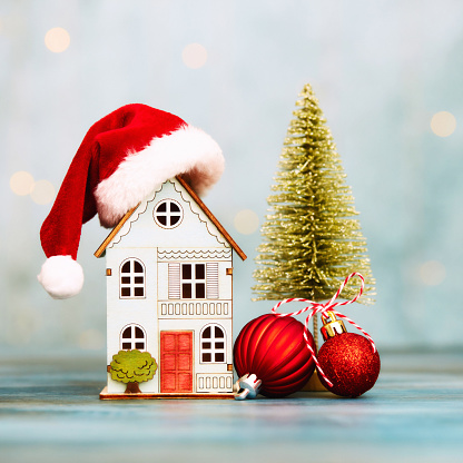 Cute wooden house wearing Santa hat with Christmas tree and Christmas ornaments. New home for Christmas. Space for text