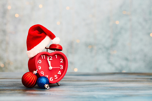 Time for Christmas. Small red alarm clock with Santa hat and Christmas decorations. Space for text
