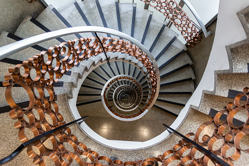 Spiral staircase with brown metal railing.  Perspective photography.  Indoor architecture.  Spiral staircase.