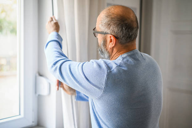 istock man standing at the window and opening the blinds 1439824774