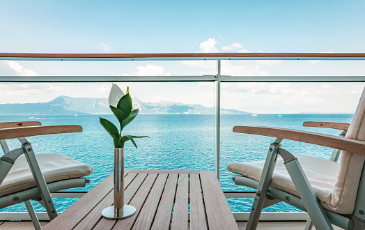 Stylish wooden outdoor table and chairs on balcony of cruise ship. Flower on the table. Sea background.