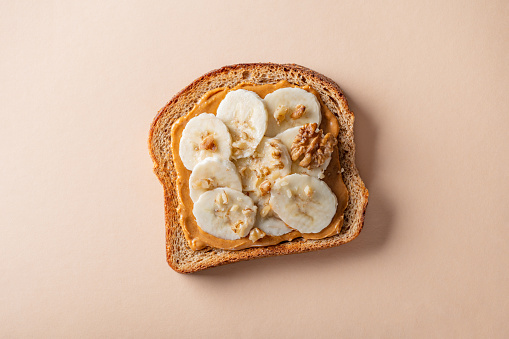 Open sandwich from slice of wholegrain bread with peanut nut butter, bananas and crushed walnuts
