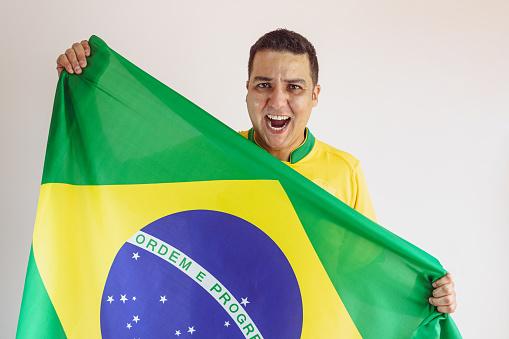 Black Man Holding Brazilian Flag With Soccer Team Yellow Shirt Isolated on White. Sport Fan Cheering for Brazil to be the champion.