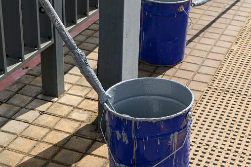 A paint roller in a metal bucket with gray paint on the street. The process of updating the streets of the city