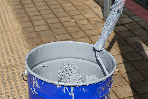 A paint roller in a metal bucket with gray paint on the street. The process of updating the streets of the city