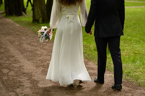 Back view of holding hands couple in love, bride and groom outdoor walking on field.