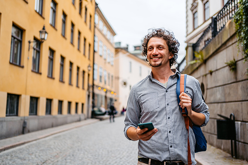 Handsome young man walking in the alley and using his smart phone in Stockholm, Sweden