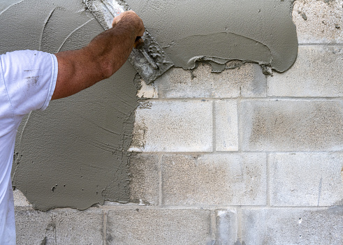A close-up of a bricklayer spreading cement on a concrete block wall.