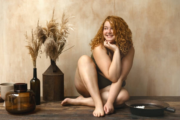 Beautiful woman in underwear Body positive model with redhead. Portrait of an attractive and voluptuous young woman posing in her lingerie against a beige background in studio plus size boho clothing stock pictures, royalty-free photos & images