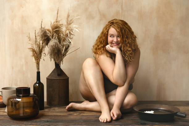 Beautiful woman in underwear Body positive model with redhead. Portrait of an attractive and voluptuous young woman posing in her lingerie against a beige background in studio plus size boho clothing stock pictures, royalty-free photos & images