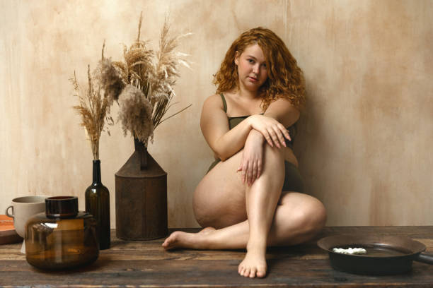 Beautiful woman in underwear Body positive model with redhead. Portrait of an attractive and voluptuous young woman posing in her lingerie against a beige background in studio plus size boho clothing stock pictures, royalty-free photos & images