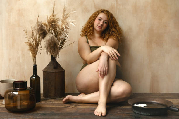 Beautiful woman in underwear Body positive model with redhead. Portrait of an attractive and voluptuous young woman posing in her lingerie against a beige background in studio plus size boho clothing stock pictures, royalty-free photos & images