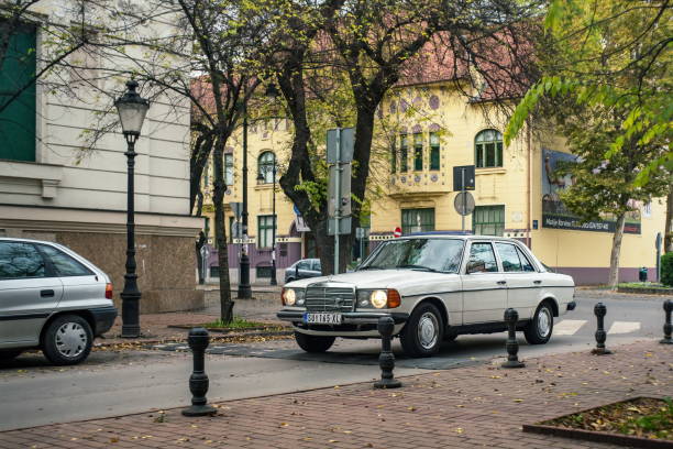 White sedan Mercedes-Benz W123 driving at historical center of european town stock photo