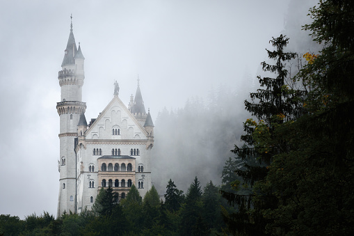 Fussen, Germany  August 19, 2022: Castle of Neuschwanstein in Fussen, stunning neo gothic palace of the XIX century and most famous landmark of Bavaria, Germany. View from afar on a rainy misty day