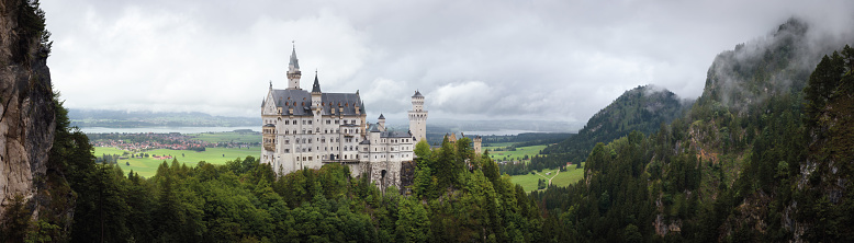Fussen, Germany  August 19, 2022: Castle of Neuschwanstein in Fussen, stunning neo gothic palace of the XIX century and most famous landmark of Bavaria, Germany. View from Marienbrucke bridge on a rainy cloudy day