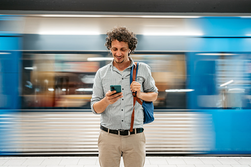 Handsome young man using his smart phone to kill time while waiting for a subway train.