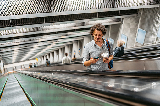 Handsome young man, holding a cup of coffee and using a smart phone on a subway escalator in Stockholm, Sweden.