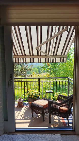 Looking out from the bedroom to the patio and garden with giant sunflowers. Wicker furniture and rug on deck. Awning down to keep bedroom cool.  Vanilla Marigolds in pots.