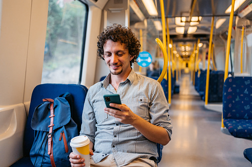 Handsome young man using phone and drinking coffee in a subway train in Stockholm.