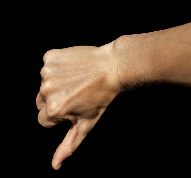 a young man's hand on an isolated black background in close-up lowers his thumb down, expressing rejection, disapproval, dislike and a negative sign. - disaffection imagens e fotografias de stock