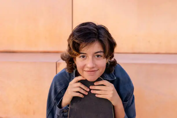 Portrait of a young, brunette short hair, woman sitting outdoors holding a skateboard portrait