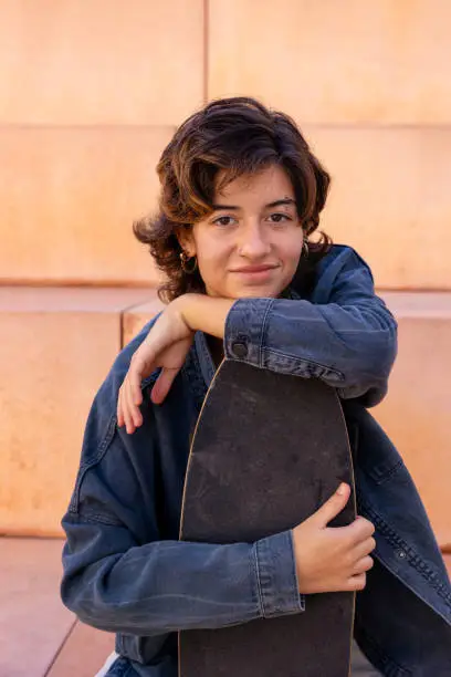 Portrait of a young, brunette short hair, woman sitting outdoors holding a skateboard portrait
