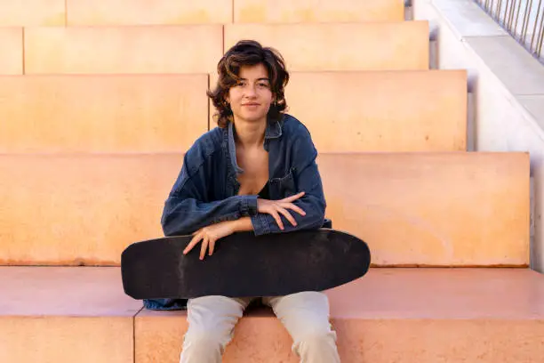 Portrait of a young, brunette short hair, woman sitting outdoors holding a skateboard portrait