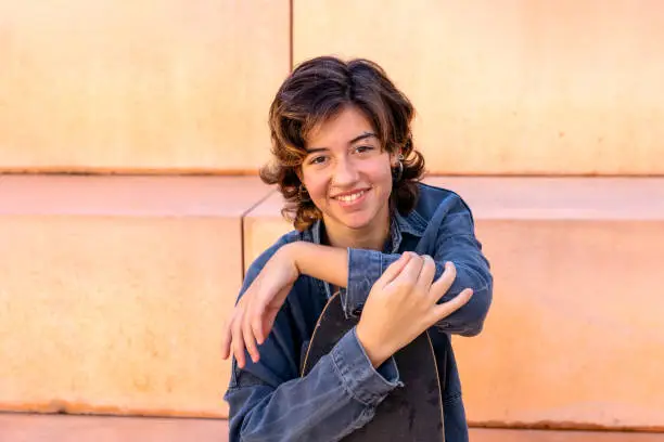 Portrait of a young, brunette short hair, woman sitting outdoors holding a skateboard portrait