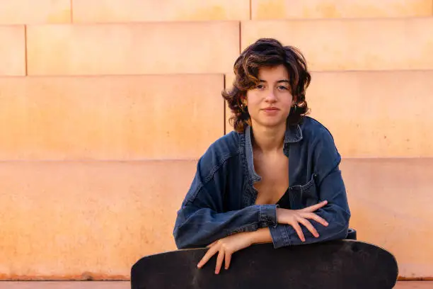 Portrait of a young, brunette short hair, woman sitting outdoors holding a skateboard portrait