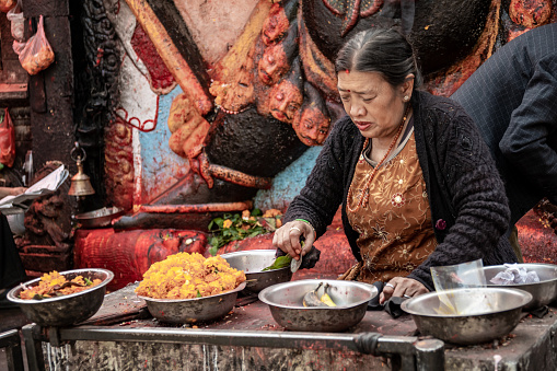 Kathmandu, Nepal - nov 6, 2019: a Nepalese woman prepares bowls for offerings to the terrible deity Kala Bhairava, whose depiction is found in Durbar Square in Kathmandu,