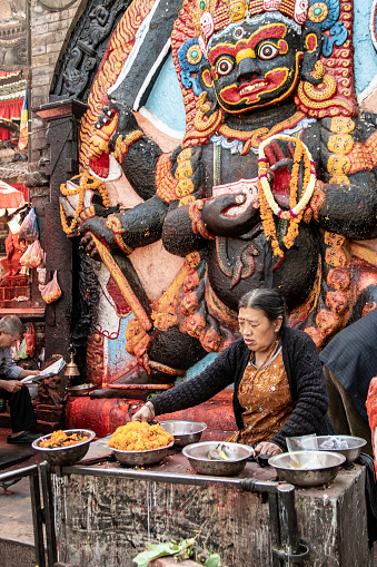Kathmandu, Nepal - nov 6, 2019: a Nepalese woman prepares bowls for offerings to the terrible deity Kala Bhairava, whose depiction is found in Durbar Square in Kathmandu,