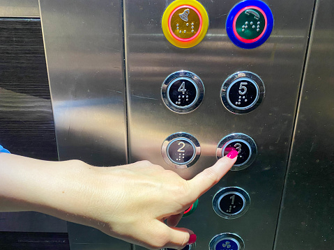 A woman's manicured finger on her hand presses a button in a modern beautiful elevator in a high-rise building.