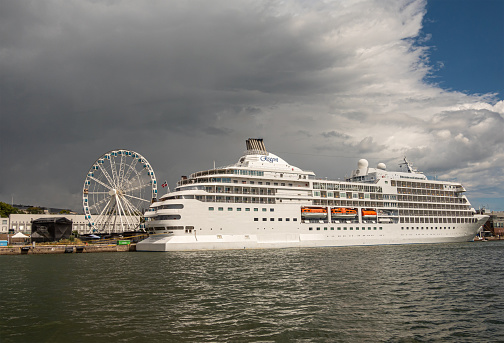 Helsinki, Finland - July 19, 2022: White Regent Seven Seas Navigator docked in port under rainy. dark sky. White skywheel in back