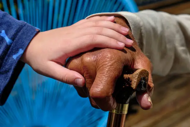 Grandchild holding grandparent's hand. Grandfather leaning on a walking stick. Dark skin toned grandfather with light skin toned grandchild.
Mixed race family.
