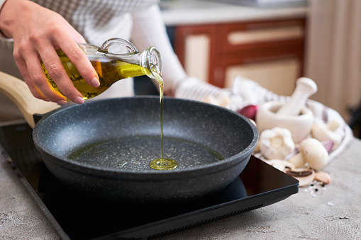 Woman pouring olive oil on frying pan at domestic kitchen.