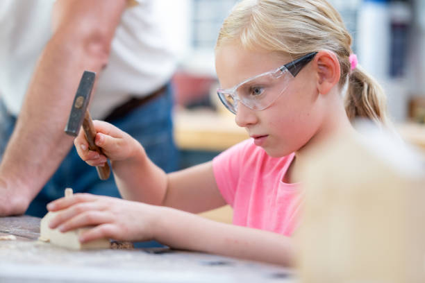 Girl in protective eyewear using hammer in handcraft class Girl in protective eyewear using hammer in handcraft class, side view. Kid making wooden toy in carpentry workshop, medium shot girl with a hammer stock pictures, royalty-free photos & images