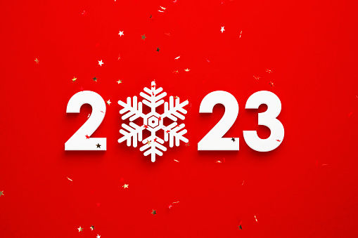White snowflake forming 2023 beneath star shaped gold confetti over red background. Horizontal composition with copy space. Directly above. Great use for 2023 concepts.