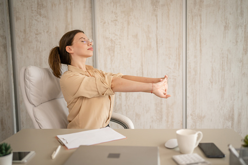 One woman female caucasian entrepreneur businesswoman or secretary sitting in office at desk at work stretching hands try to relax shoulders and back wear shirt copy space