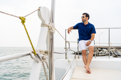 Caucasian businessman in casual clothing talking on mobile phone for corporate business while travel on luxury catamaran boat yacht sailing in the ocean on summer holiday vacation.