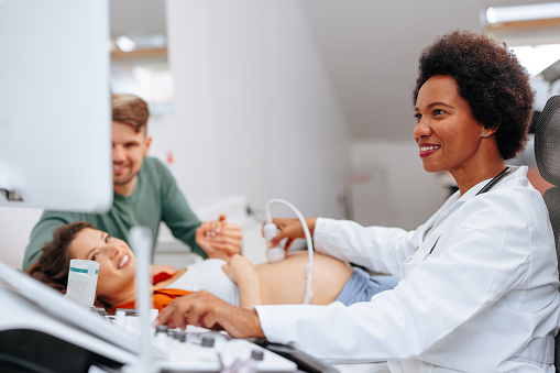 An African American female gynecologist is at her office doing an ultrasound checkup on a young woman with her husband.