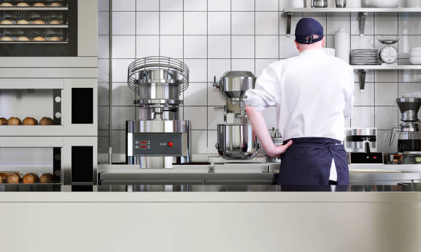 Male professional baker working in industrial bakery kitchen with empty stainless steel counter for product display