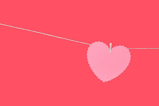 Pink heart hanging on string against coral red background with copy space