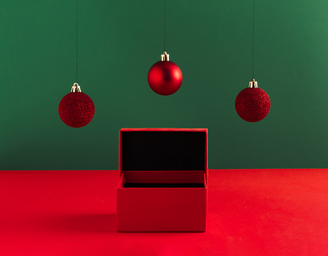 Creative Christmas concept made of gift box and red baubles on bold green background. Minimal New Year advertisement concept. Mock up showcase for product, promotion, sale or presentation.