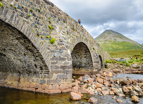 Sligachan,Isle of Skye,Scotland,United Kingdom-July 27 2022:A visitor to the historic Skye site,perches on the ancient bridge,looking towards the Black Cullin mountains,on a mid summer day.