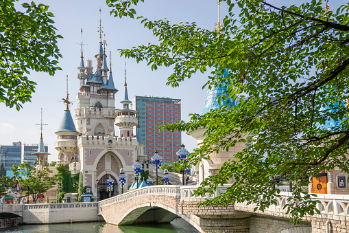 Seoul, South Korea - July 26, 2022: Green leaves   from a cherry tree frame a castle at Lotte World's Magic Island in the middle of Seokchon Lake in Jamsil.