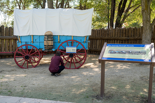 Genoa, NV. Unidentified young man looking at a blue Prairie Schooner wagon with red wheels at the Mormon Station Historic Park.